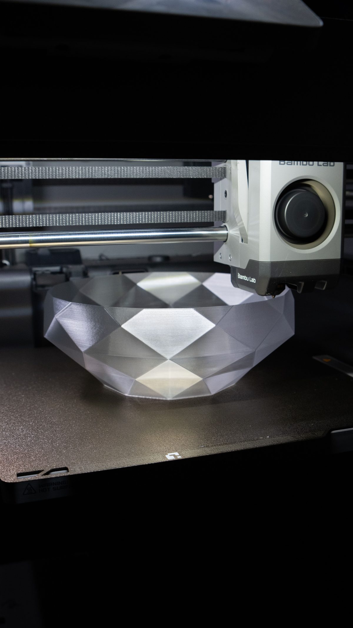 A Bambu Lab 3D printer mid-print, producing a faceted bowl